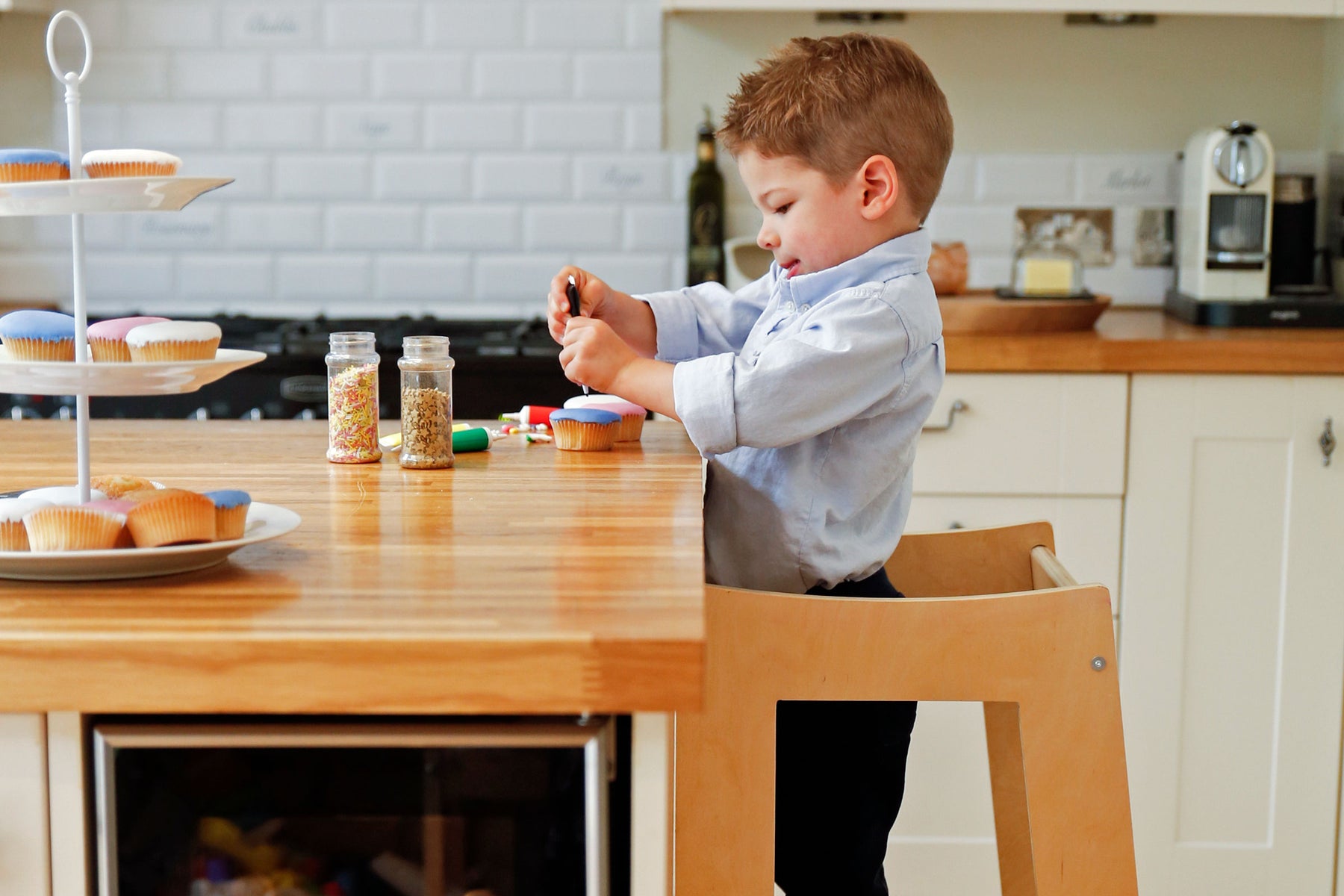 Picture of a child in the Stepup Baby Toddler Tower baking and decorating cakes at the kitchen counter.  In a safe way with adjustable height platform 